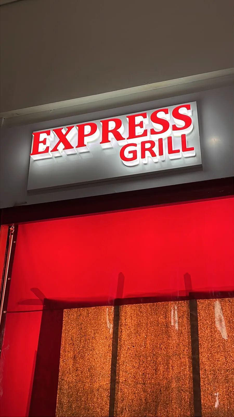 Letreiro Express Grill visto de frente, com letras vermelhas iluminadas